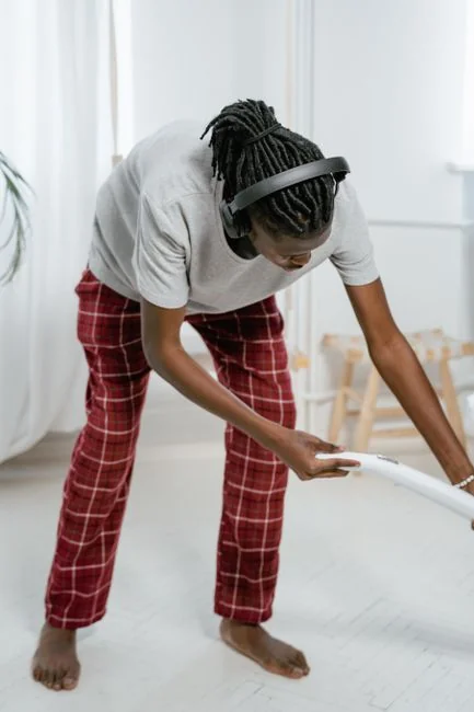 Une femme adulte en combinaison rouge utilise un aspirateur dans un intérieur moderne, concentrée sur des tâches de nettoyage.